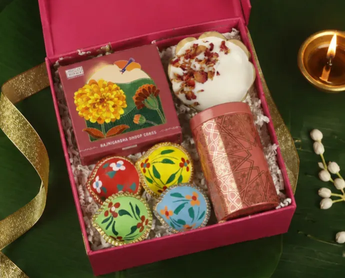Close-up of fluorescent Diwali box contents including patterned tea tin and hand-painted clay diyas